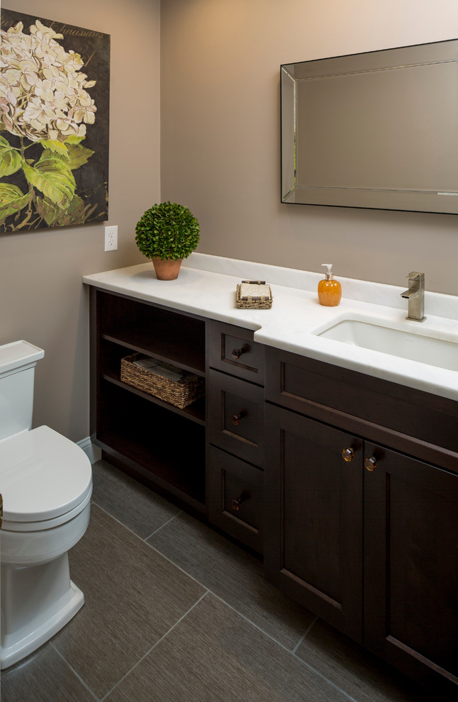 Photo of a mid-sized transitional powder room in Philadelphia with flat-panel cabinets, dark wood cabinets, a two-piece toilet, beige walls, ceramic floors, marble benchtops, gray tile and an undermount sink.