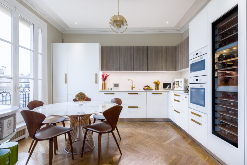 Inspiration pour une cuisine américaine encastrable design en L avec un placard à porte plane, des portes de placard blanches, une crédence blanche, un sol en bois brun, aucun îlot, un sol marron et un plan de travail blanc.