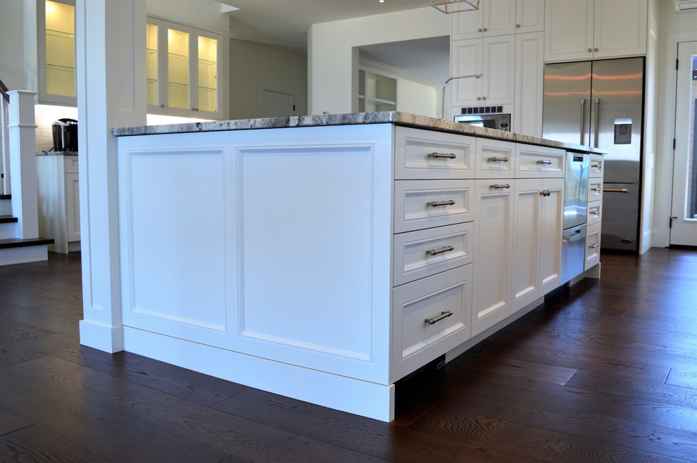 Expansive traditional l-shaped eat-in kitchen in Toronto with an undermount sink, shaker cabinets, white cabinets, granite benchtops, white splashback, ceramic splashback, stainless steel appliances, dark hardwood floors, with island, brown floor and multi-coloured benchtop.
