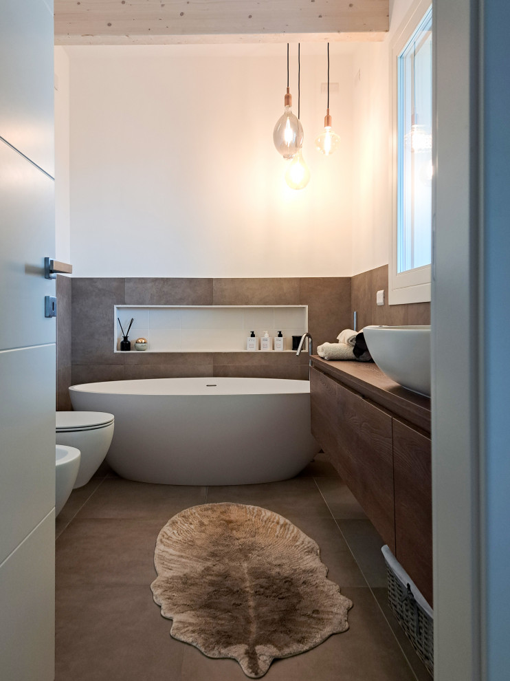 Стильный дизайн: главная ванная комната среднего размера в современном стиле с темными деревянными фасадами, отдельно стоящей ванной, душем в нише, раздельным унитазом, коричневой плиткой, керамогранитной плиткой, белыми стенами, полом из керамогранита, настольной раковиной, столешницей из дерева, коричневым полом, душем с распашными дверями, тумбой под одну раковину, подвесной тумбой и балками на потолке - последний тренд