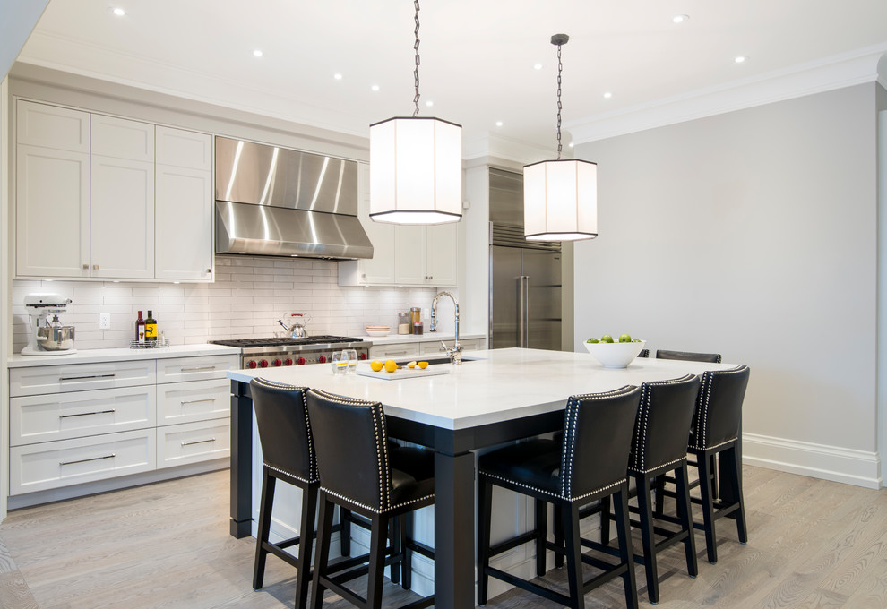 Transitional galley beige floor open concept kitchen photo in Toronto with an undermount sink, shaker cabinets, white cabinets, white backsplash, subway tile backsplash, stainless steel appliances and an island