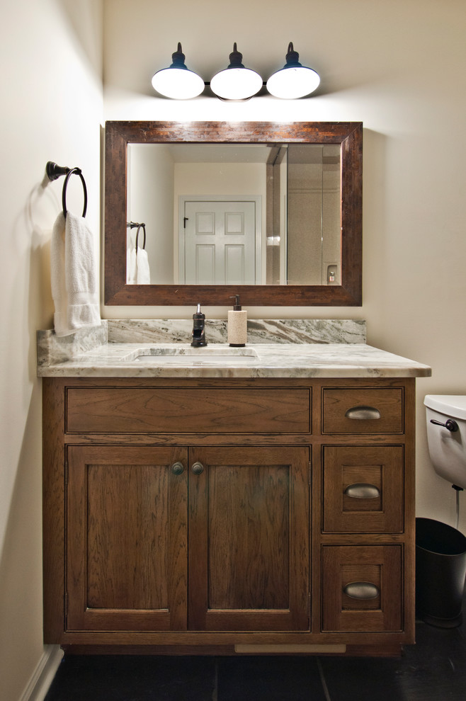 Photo of a mid-sized country 3/4 bathroom in Nashville with beaded inset cabinets, brown cabinets, a two-piece toilet, white tile, beige walls, linoleum floors, an undermount sink, quartzite benchtops and black floor.