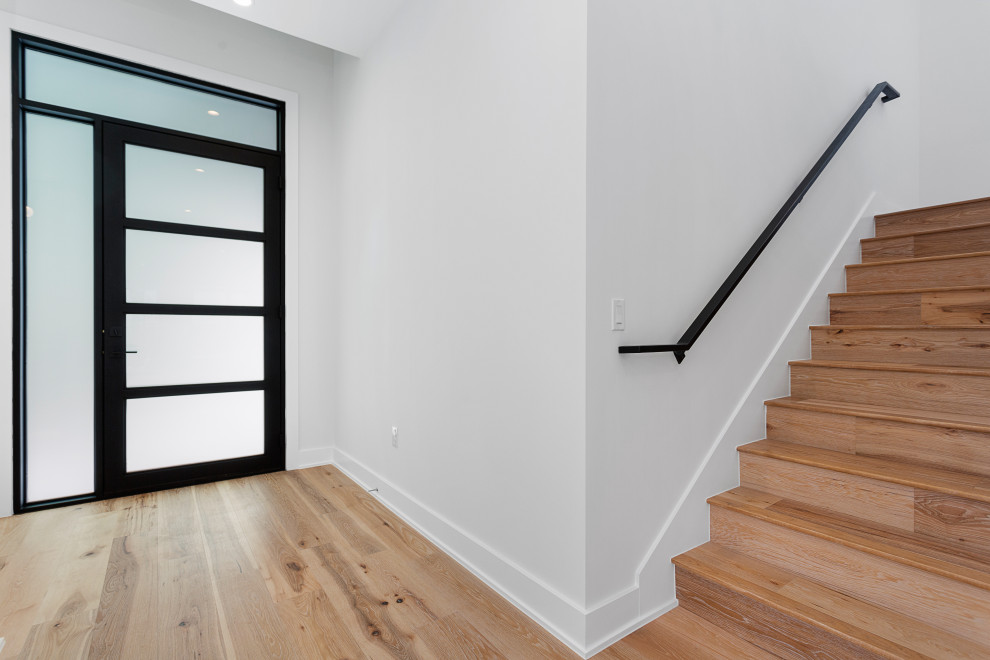 Foto på en mellanstor funkis entré, med vita väggar, ljust trägolv, en enkeldörr, en svart dörr och flerfärgat golv
