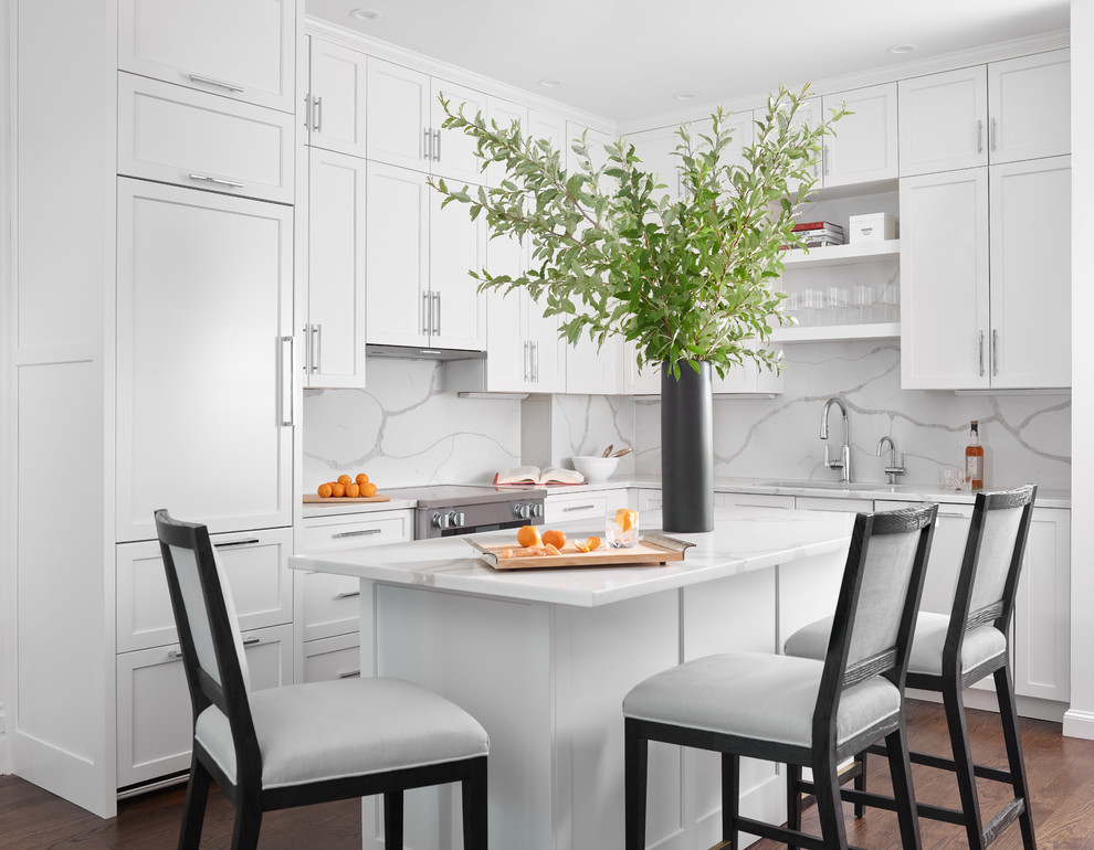 Example of a mid-sized transitional l-shaped dark wood floor and brown floor kitchen design in Boston with quartzite countertops, white backsplash, an island, white countertops, shaker cabinets, white cabinets, stone slab backsplash and paneled appliances