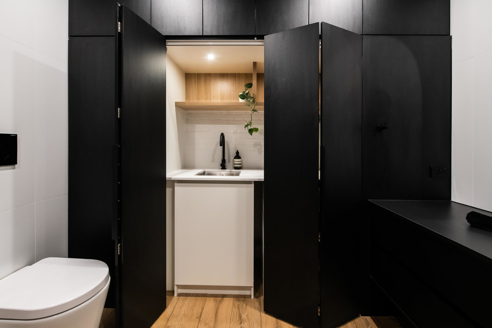 Design ideas for a large contemporary galley utility room in Melbourne with porcelain floors, brown floor, a drop-in sink, open cabinets, light wood cabinets, laminate benchtops, white walls, an integrated washer and dryer and white benchtop.