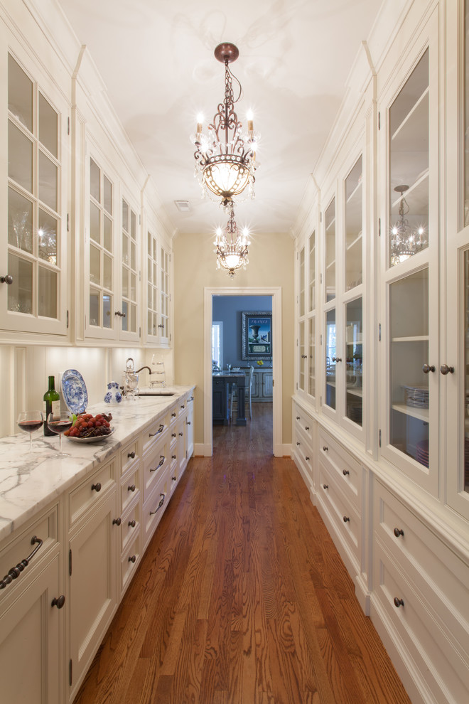 Inspiration for a large traditional galley kitchen pantry in St Louis with glass-front cabinets, white cabinets, marble benchtops, white splashback, panelled appliances and medium hardwood floors.