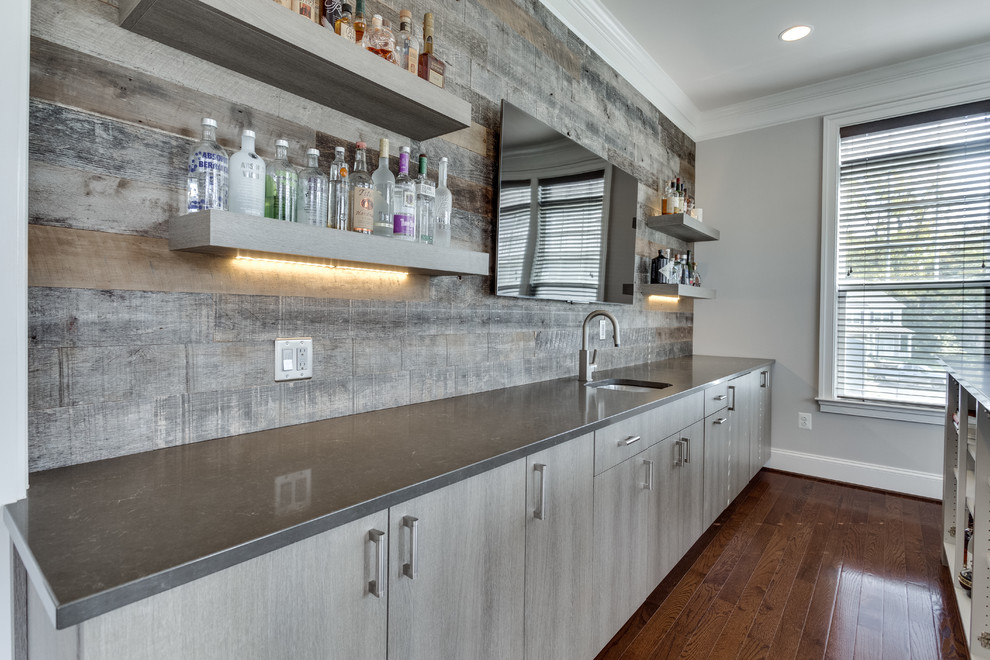 Photo of a mid-sized modern galley seated home bar in DC Metro with an undermount sink, quartz benchtops, grey splashback and medium hardwood floors.