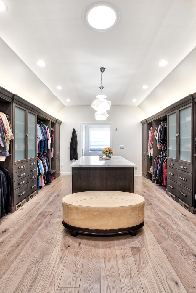 Expansive transitional gender-neutral walk-in wardrobe in New York with flat-panel cabinets, dark wood cabinets and light hardwood floors.