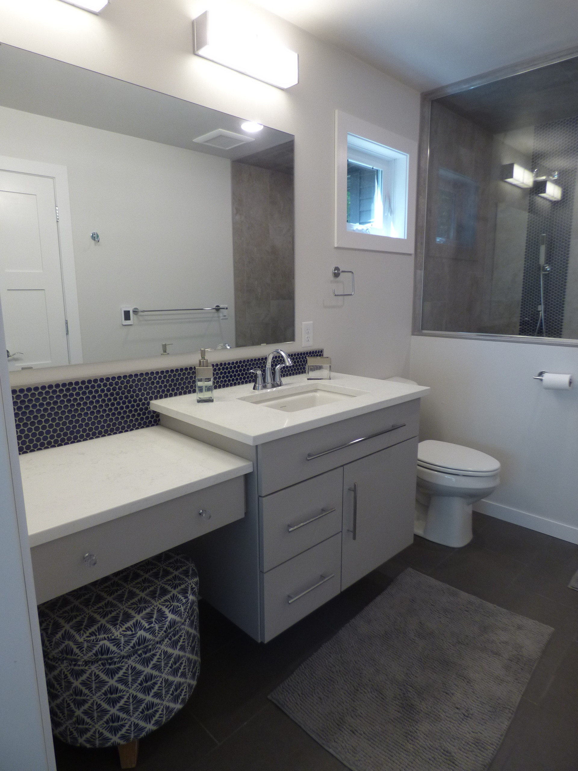 The Master Shower has a custom tile wall in large format ceramic, with a small blue honeycomb tile accent to match the floor and backsplash.  The floating vanity has a lowered makeup counter. A transo