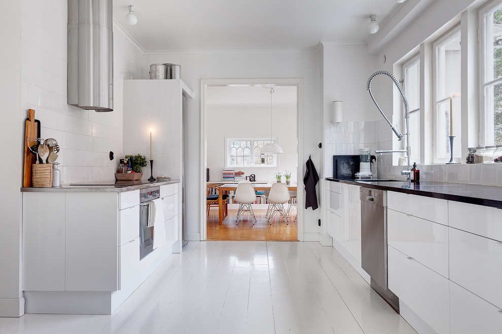 Photo of a mid-sized scandinavian galley separate kitchen in Stockholm with an undermount sink, flat-panel cabinets, white cabinets, white splashback, stainless steel appliances, painted wood floors, no island and laminate benchtops.
