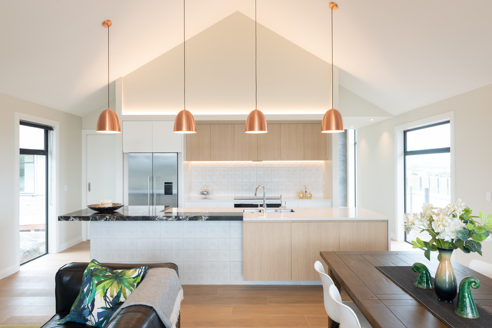 This is an example of a large contemporary galley eat-in kitchen in Christchurch with an undermount sink, light wood cabinets, quartz benchtops, white splashback, ceramic splashback, stainless steel appliances, ceramic floors, with island, flat-panel cabinets, brown floor and white benchtop.