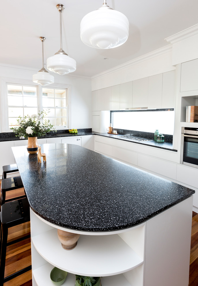 Modern l-shaped kitchen in Brisbane with white cabinets, black splashback, medium hardwood floors and with island.