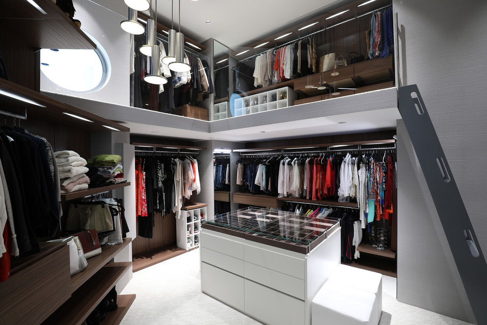 Contemporary gender-neutral walk-in wardrobe with open cabinets, brown cabinets, carpet and white floor.