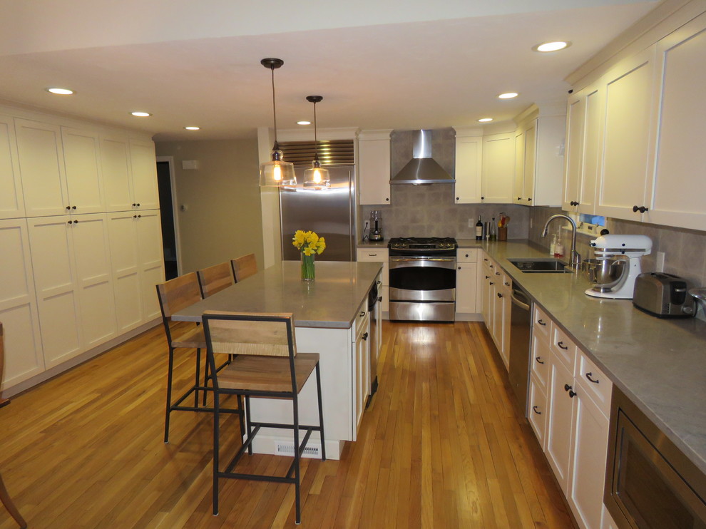 Example of a large transitional l-shaped medium tone wood floor open concept kitchen design in Boston with an undermount sink, shaker cabinets, white cabinets, quartz countertops, gray backsplash, stainless steel appliances and an island