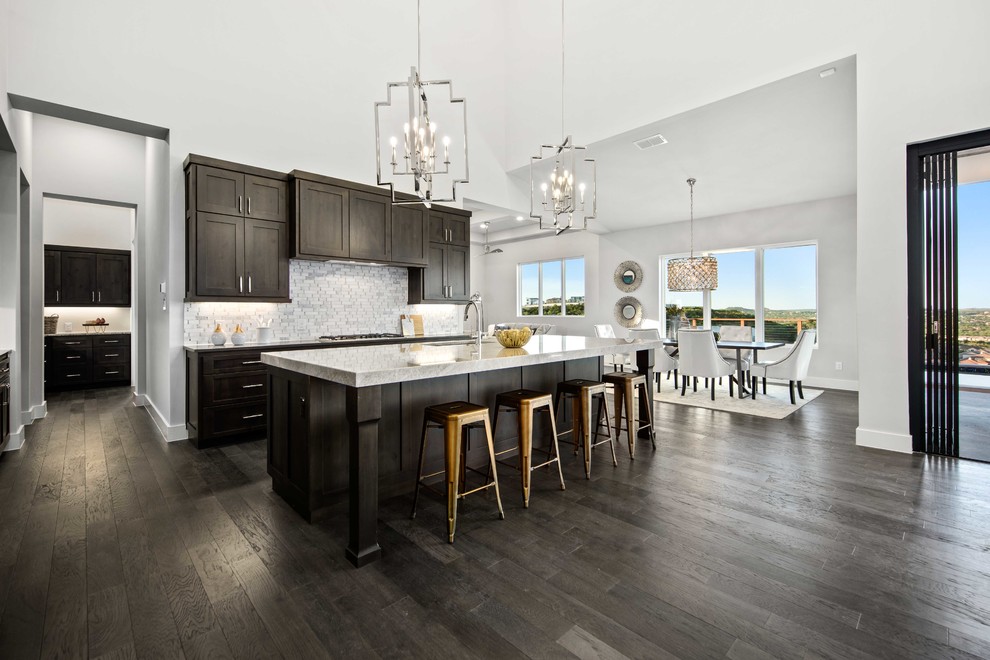This is an example of a large transitional u-shaped eat-in kitchen in Austin with an undermount sink, shaker cabinets, dark wood cabinets, quartzite benchtops, white splashback, marble splashback, stainless steel appliances, dark hardwood floors, with island, brown floor and grey benchtop.