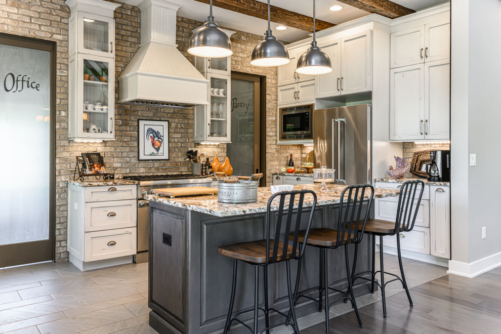 Design ideas for a country open plan kitchen in Other with raised-panel cabinets, distressed cabinets, granite benchtops, brown splashback, brick splashback, stainless steel appliances, ceramic floors, with island, grey floor, brown benchtop and exposed beam.