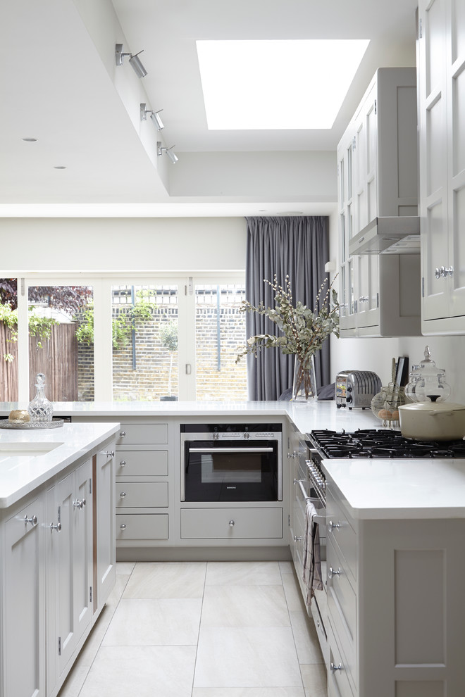 Traditional l-shaped kitchen in London with an undermount sink, shaker cabinets, white cabinets, with island and stainless steel appliances.