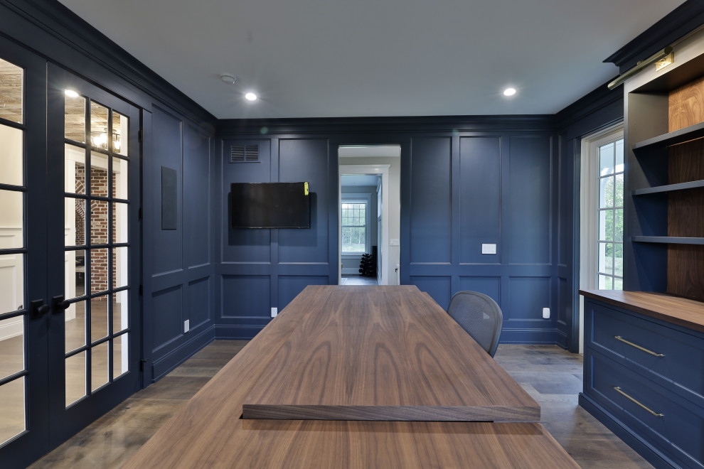 Inspiration for a large country home office in Philadelphia with a library, a built-in desk, blue walls, dark hardwood floors, brown floor and decorative wall panelling.