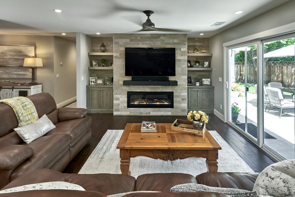 Inspiration for a large transitional open concept family room in San Francisco with grey walls, dark hardwood floors, a standard fireplace, a stone fireplace surround, a wall-mounted tv and brown floor.