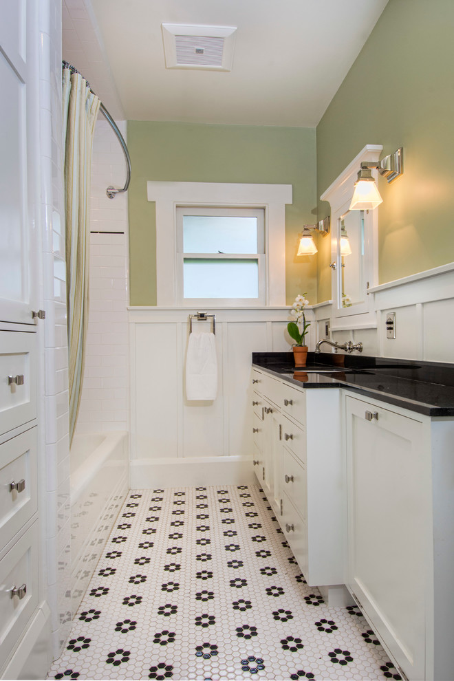 This is an example of an arts and crafts bathroom in Los Angeles with shaker cabinets, an alcove tub, a shower/bathtub combo, a two-piece toilet, white tile, ceramic tile, green walls, ceramic floors, an undermount sink, granite benchtops, white floor, a shower curtain and black benchtops.
