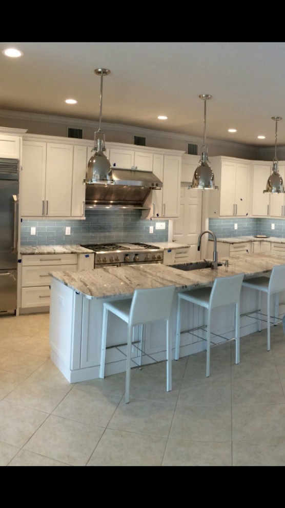 Photo of a large beach style l-shaped open plan kitchen in Tampa with an undermount sink, shaker cabinets, white cabinets, granite benchtops, blue splashback, glass tile splashback, stainless steel appliances, porcelain floors and with island.