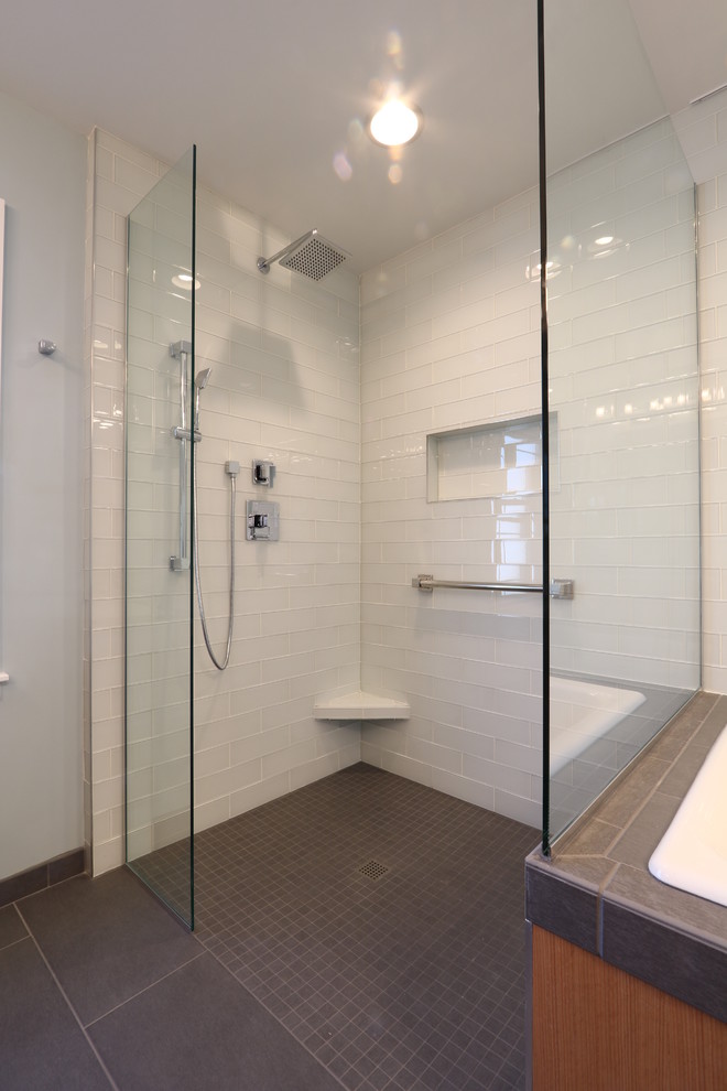 This is an example of a mid-sized contemporary master bathroom in Other with flat-panel cabinets, medium wood cabinets, a drop-in tub, a curbless shower, a one-piece toilet, white tile, glass tile, blue walls, porcelain floors, an integrated sink and solid surface benchtops.