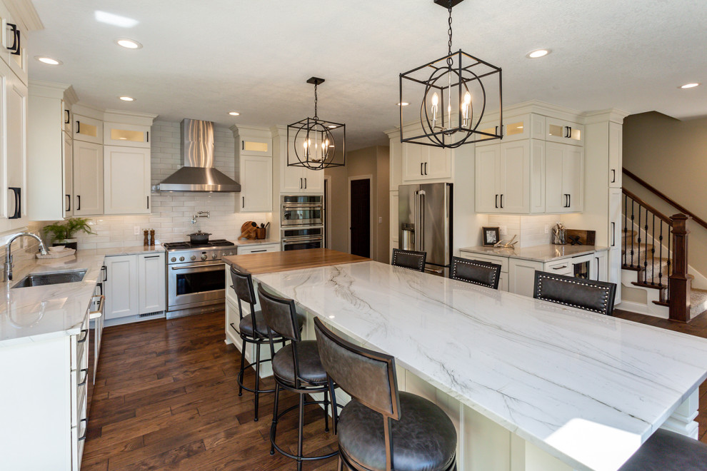 Example of a large transitional u-shaped medium tone wood floor and brown floor kitchen design in Other with a single-bowl sink, recessed-panel cabinets, white cabinets, quartzite countertops, white backsplash, glass tile backsplash, stainless steel appliances, an island and white countertops