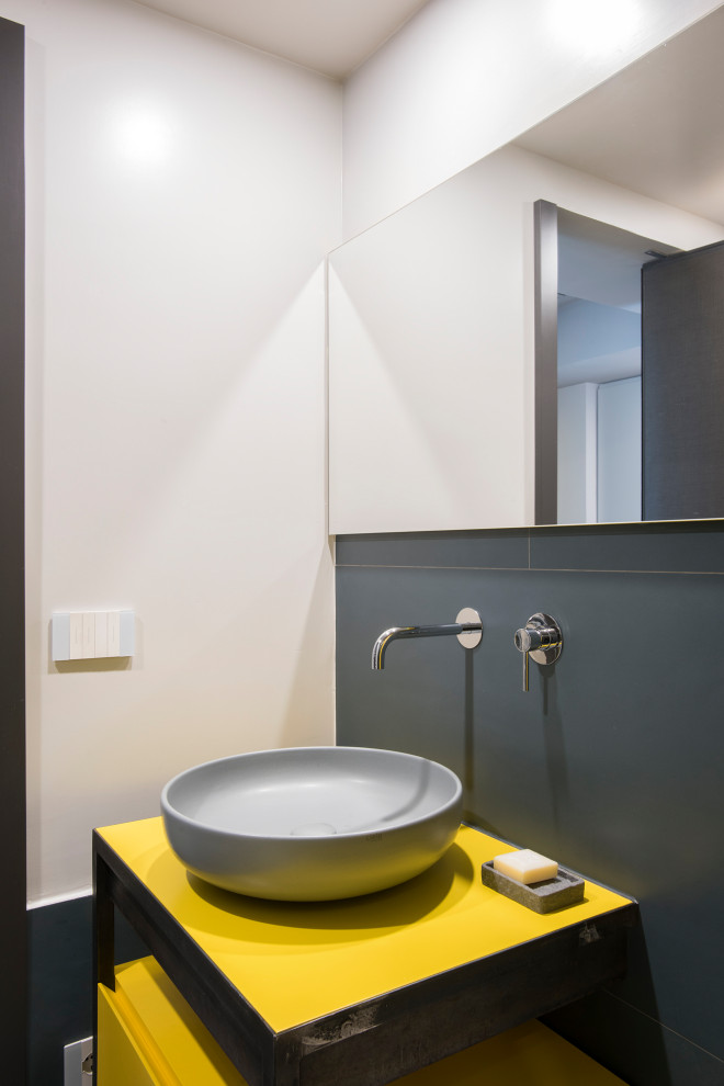 This is an example of an eclectic bathroom in Rome with furniture-like cabinets, yellow cabinets, a wall-mount toilet, porcelain floors, a vessel sink, grey floor, a sliding shower screen and yellow benchtops.