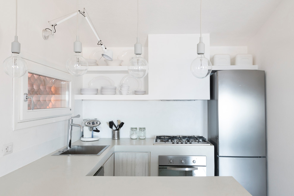 Small beach style u-shaped kitchen in Other with an undermount sink, raised-panel cabinets, white cabinets, concrete benchtops, white splashback, stainless steel appliances and a peninsula.