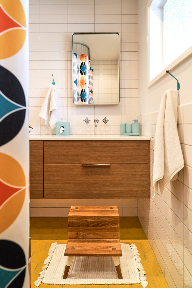 Design ideas for a medium sized midcentury family bathroom in San Diego with flat-panel cabinets, medium wood cabinets, a corner bath, a shower/bath combination, a one-piece toilet, white tiles, metro tiles, white walls, porcelain flooring, a submerged sink, engineered stone worktops, yellow floors, a shower curtain, white worktops, double sinks and a built in vanity unit.