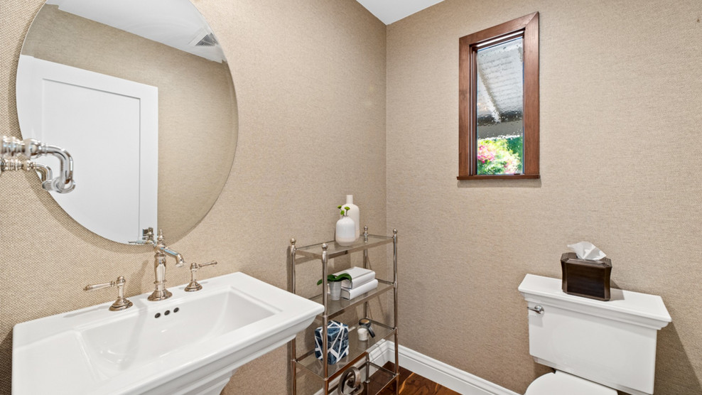 This is an example of an expansive transitional powder room in Los Angeles with a wall-mount toilet, medium hardwood floors, a pedestal sink and brown floor.