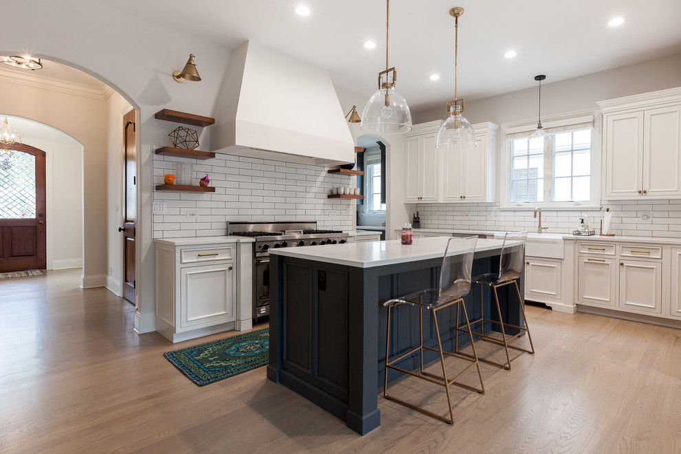 This is an example of an expansive transitional u-shaped eat-in kitchen in Chicago with a farmhouse sink, beaded inset cabinets, white cabinets, quartz benchtops, white splashback, ceramic splashback, stainless steel appliances, medium hardwood floors, with island, grey floor and white benchtop.