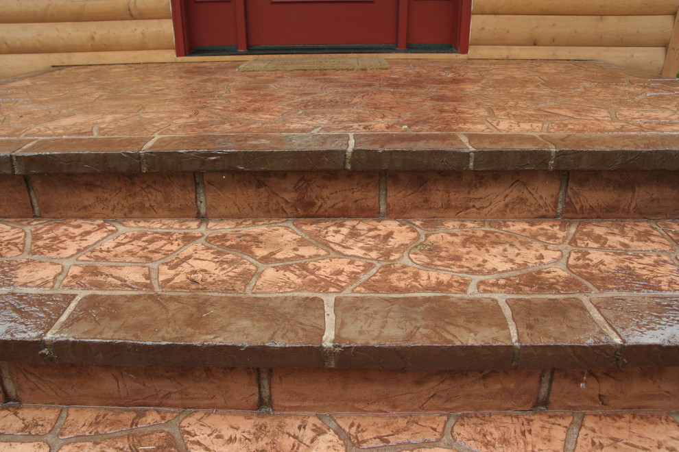 Example of a mid-sized mountain style front yard stamped concrete home design design with a roof extension