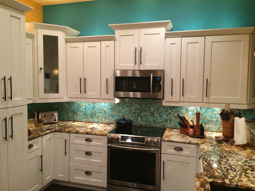 Photo of a large tropical u-shaped eat-in kitchen in Miami with shaker cabinets, white cabinets, granite benchtops, blue splashback, glass tile splashback, stainless steel appliances, bamboo floors and no island.
