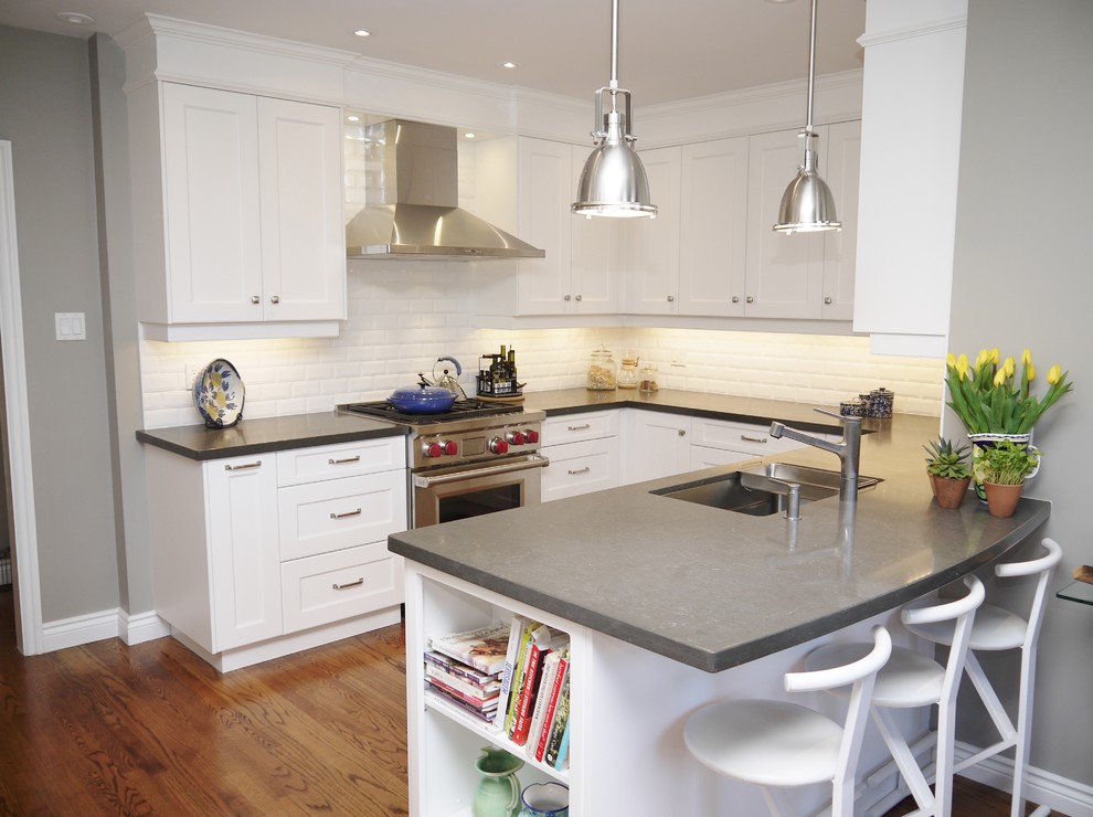 Eat-in kitchen - mid-sized transitional u-shaped medium tone wood floor eat-in kitchen idea in Toronto with an undermount sink, recessed-panel cabinets, white cabinets, quartz countertops, white backsplash, porcelain backsplash, stainless steel appliances and a peninsula