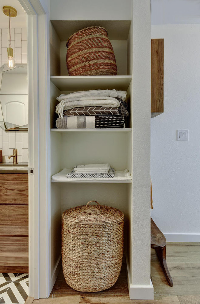 Photo of a small modern gender-neutral built-in wardrobe in Austin with open cabinets, white cabinets and light hardwood floors.