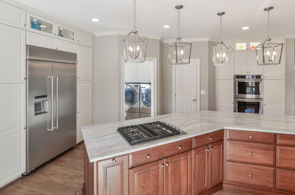 Photo of a large traditional kitchen in DC Metro with an undermount sink, raised-panel cabinets, granite benchtops, grey splashback, stainless steel appliances, medium hardwood floors, with island and grey benchtop.