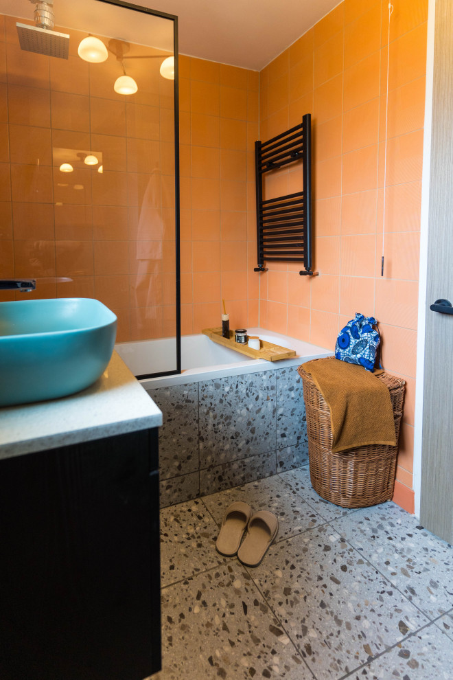 Пример оригинального дизайна: маленькая детская ванная комната в стиле фьюжн с накладной ванной, душем над ванной, унитазом-моноблоком, оранжевой плиткой, керамической плиткой, разноцветными стенами, накладной раковиной, столешницей из ламината, серым полом, серой столешницей, нишей, тумбой под одну раковину, стеклянными фасадами, темными деревянными фасадами, встроенной тумбой и полом из терраццо для на участке и в саду