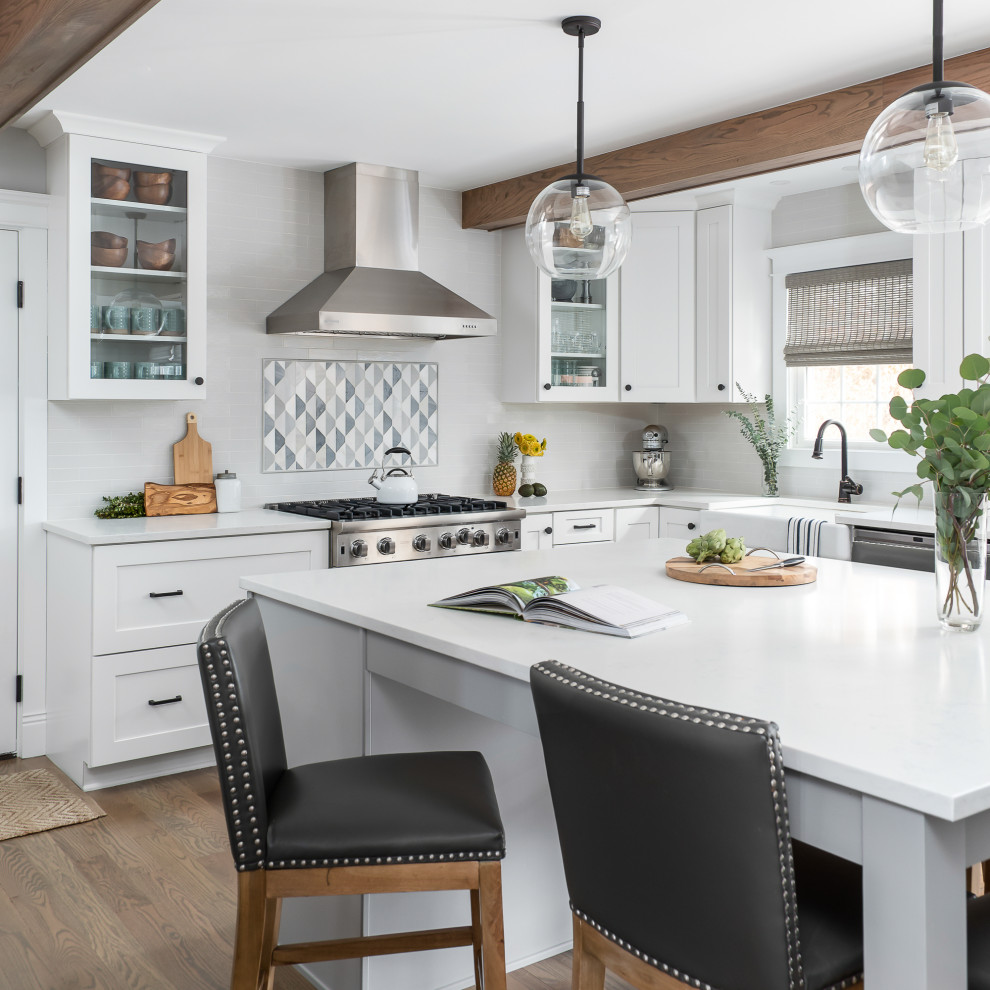 Large rural kitchen/diner in Chicago with a belfast sink, white splashback, stainless steel appliances, light hardwood flooring, an island, brown floors and exposed beams.