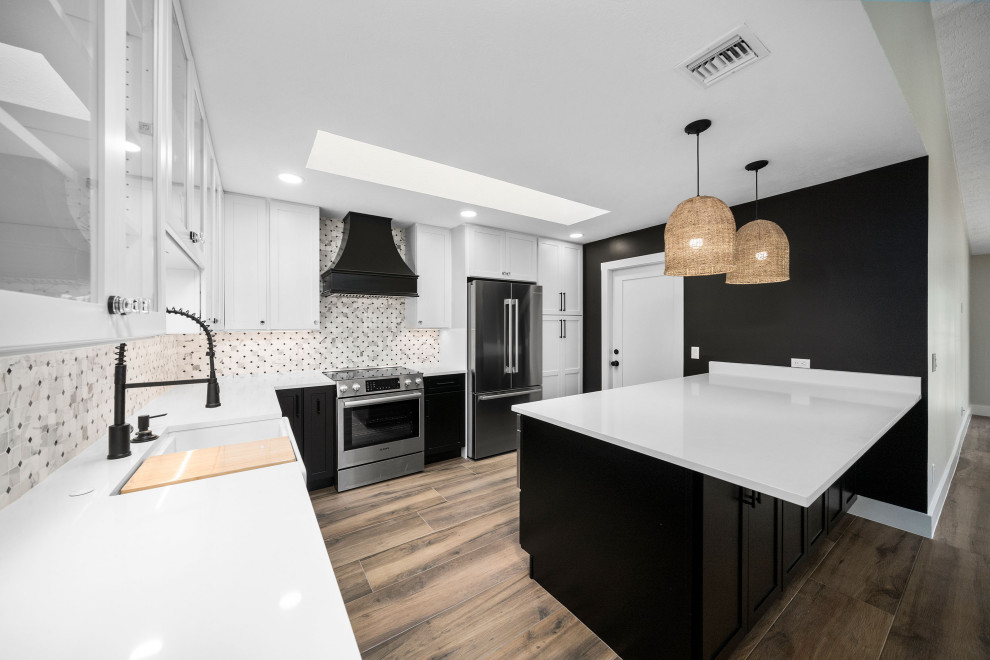 Design ideas for a mid-sized modern l-shaped eat-in kitchen in Atlanta with a farmhouse sink, shaker cabinets, black cabinets, granite benchtops, white splashback, granite splashback, stainless steel appliances, painted wood floors, with island and brown floor.