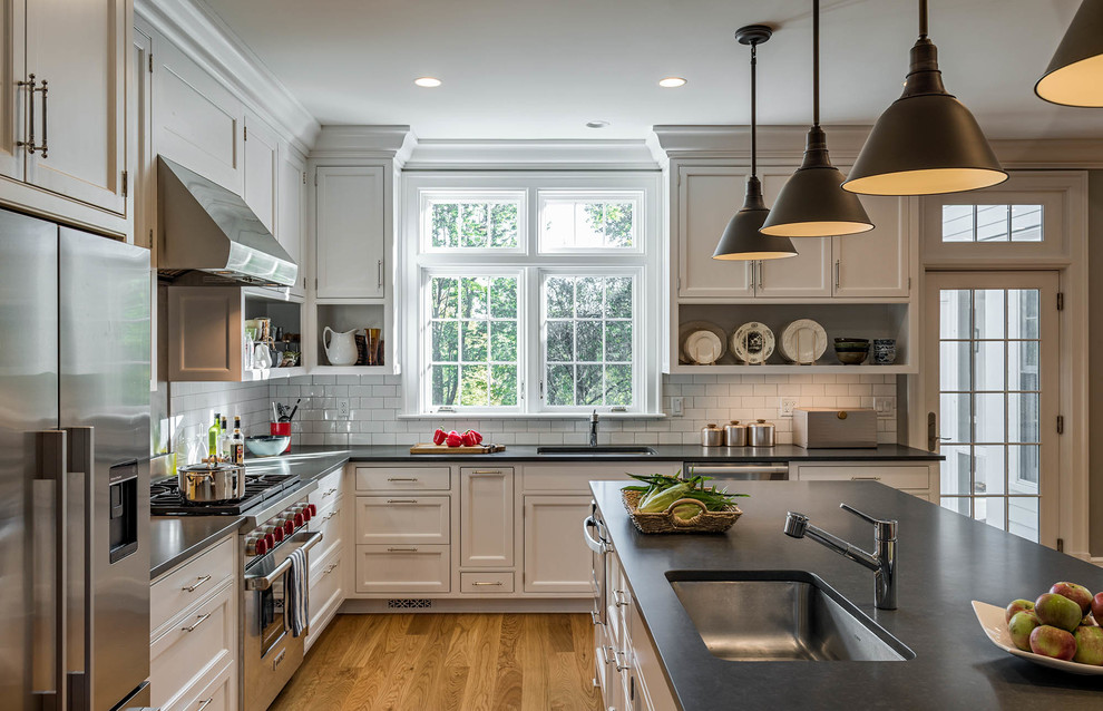 This is an example of a large traditional u-shaped kitchen in New York with an undermount sink, flat-panel cabinets, white cabinets, soapstone benchtops, white splashback, subway tile splashback, stainless steel appliances, medium hardwood floors and with island.