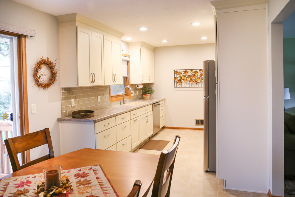 This is an example of a small transitional galley separate kitchen in Minneapolis with an integrated sink, shaker cabinets, white cabinets, laminate benchtops, beige splashback, glass tile splashback, stainless steel appliances, vinyl floors and no island.