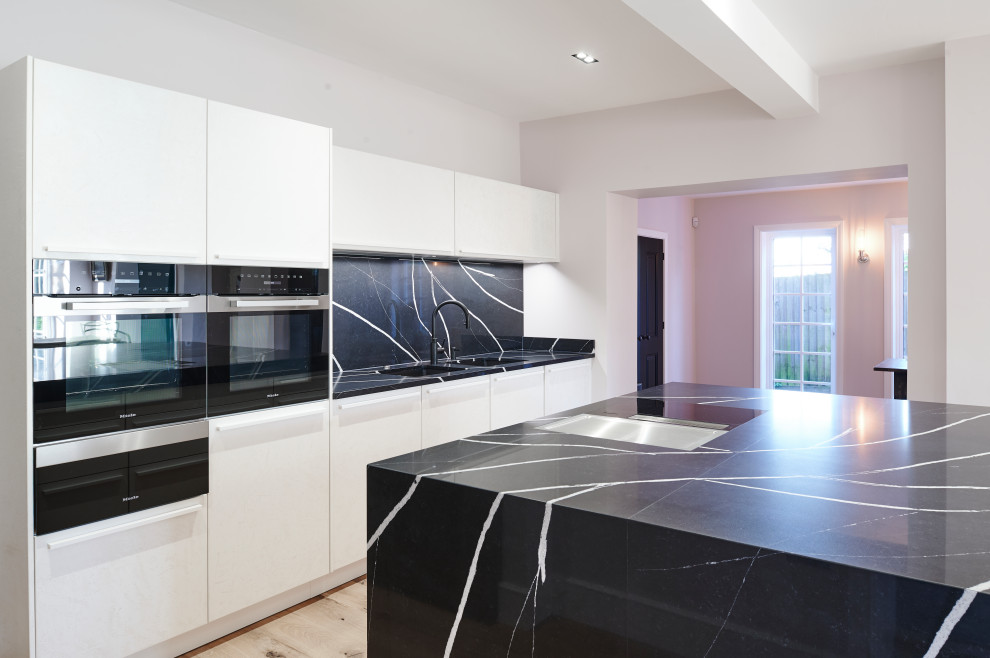 Inspiration for a mid-sized contemporary open plan kitchen in Other with white cabinets, quartzite benchtops, black splashback, with island and black benchtop.