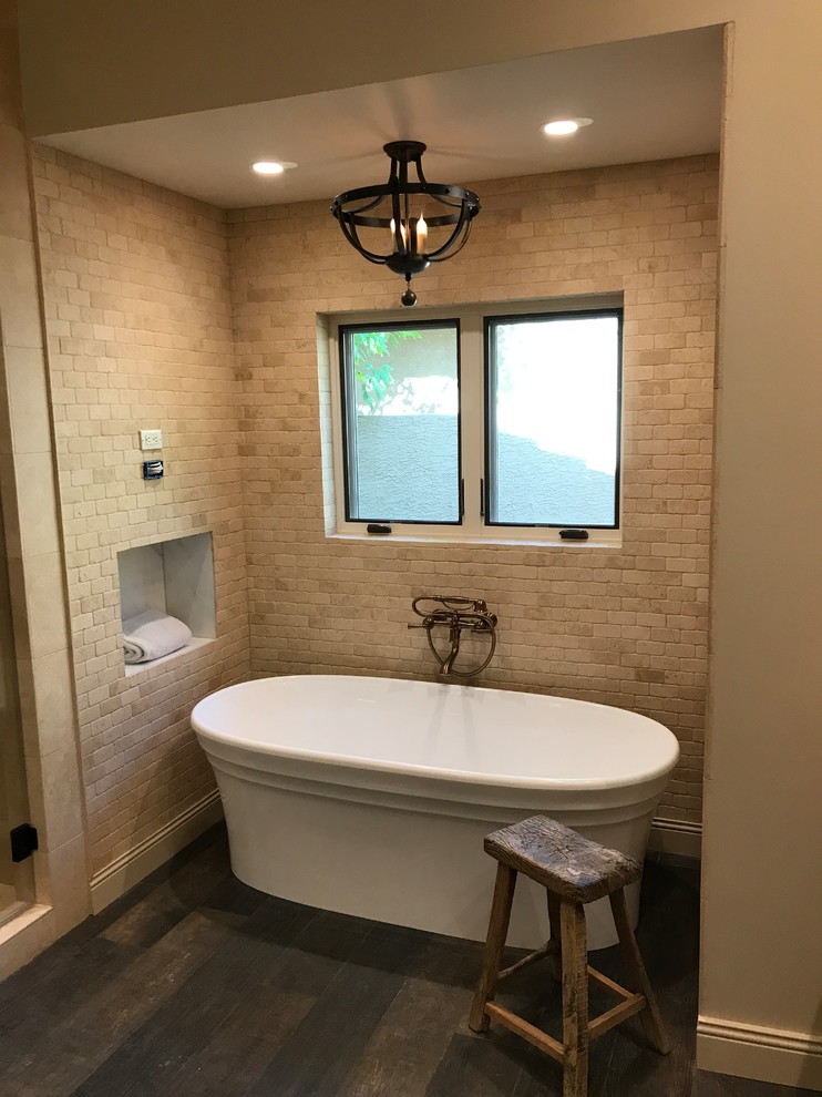 Inspiration for a mid-sized mediterranean master bathroom in Phoenix with raised-panel cabinets, dark wood cabinets, a freestanding tub, an alcove shower, a one-piece toilet, beige tile, stone tile, beige walls, dark hardwood floors, a vessel sink, marble benchtops, brown floor and a hinged shower door.