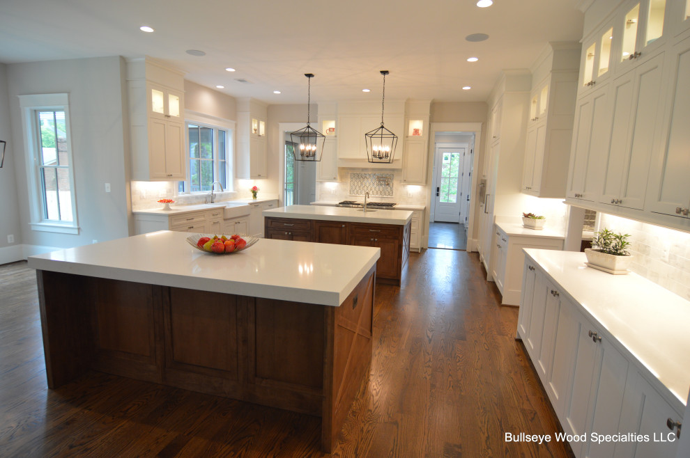 Inspiration for an expansive traditional u-shaped open plan kitchen in DC Metro with a belfast sink, shaker cabinets, medium wood cabinets, engineered stone countertops, white splashback, integrated appliances, medium hardwood flooring, multiple islands, brown floors and white worktops.
