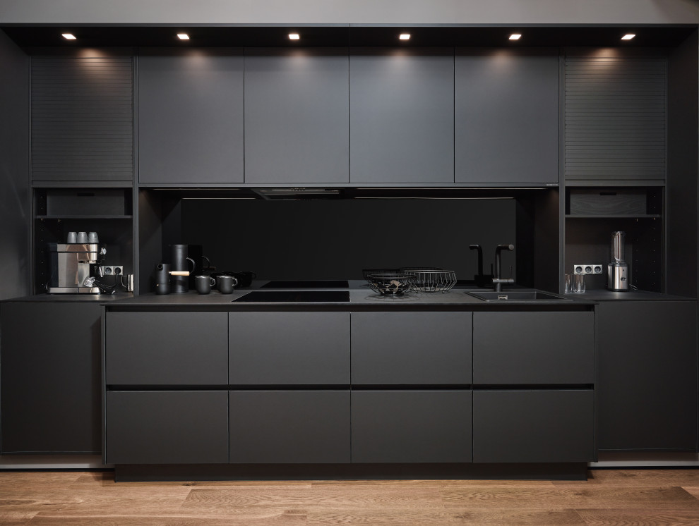 Small industrial galley separate kitchen in Atlanta with a drop-in sink, flat-panel cabinets, black cabinets, laminate benchtops, black splashback, timber splashback, black appliances, medium hardwood floors, no island, brown floor, black benchtop and coffered.