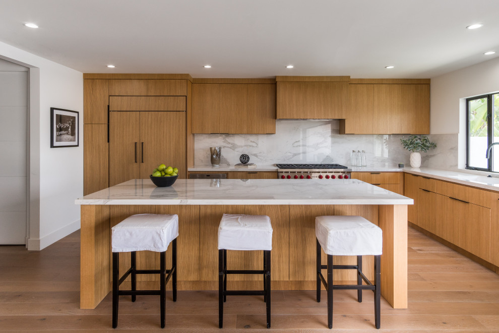 Design ideas for a midcentury l-shaped kitchen in Los Angeles with flat-panel cabinets, light wood cabinets, white splashback, stone slab splashback, light hardwood floors, with island, beige floor, white benchtop and panelled appliances.