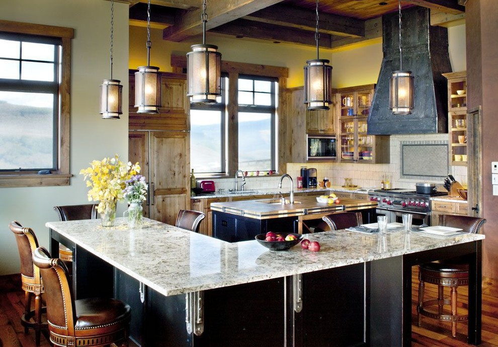 Example of a large mountain style l-shaped medium tone wood floor open concept kitchen design in Denver with a single-bowl sink, raised-panel cabinets, medium tone wood cabinets, granite countertops, beige backsplash, stone tile backsplash, stainless steel appliances and two islands