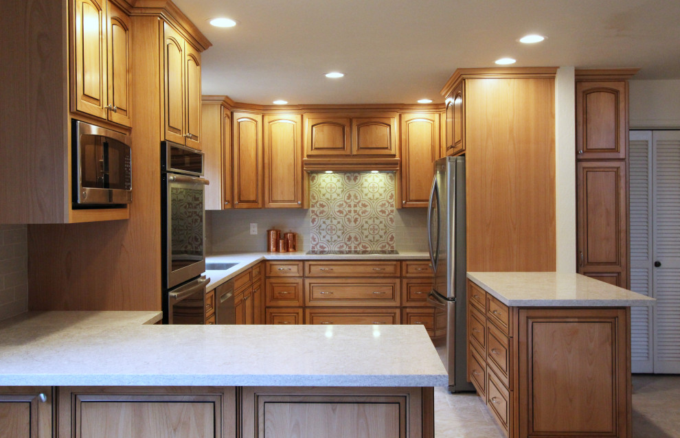 Eat-in kitchen - mid-sized u-shaped porcelain tile and beige floor eat-in kitchen idea with an undermount sink, raised-panel cabinets, medium tone wood cabinets, quartz countertops, multicolored backsplash, ceramic backsplash, stainless steel appliances, a peninsula and multicolored countertops
