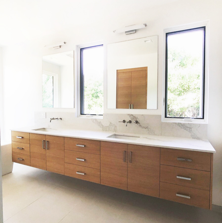 Photo of a large contemporary master bathroom in Santa Barbara with flat-panel cabinets, light wood cabinets, a curbless shower, a one-piece toilet, white walls, pebble tile floors, an undermount sink, engineered quartz benchtops, multi-coloured floor, a hinged shower door, multi-coloured benchtops, an enclosed toilet, a double vanity and a floating vanity.